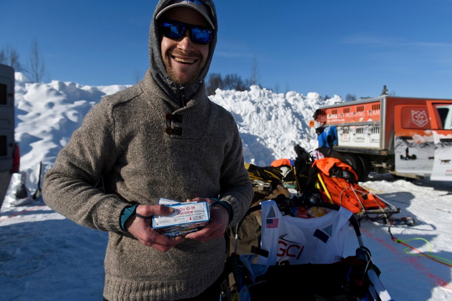 A man holding small boxes that say "COVID--19 Vaccine" stands near loaded sleds.