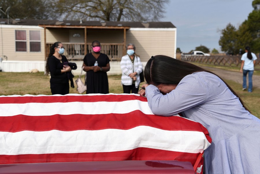 A woman leans on a coffin that is draped in an American flag, as several others look on.