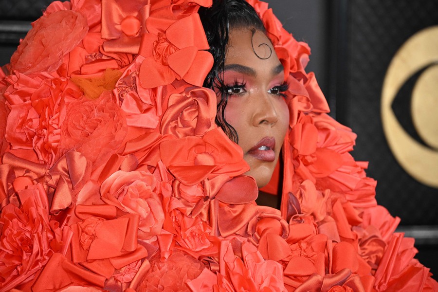 The performer Lizzo stands for photographs, wearing a large red garment that covers her head.