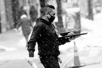 A restaurant server holds a tray while walking outside in the snow.