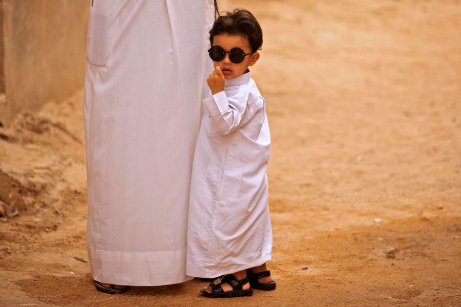 A young boy wearing sunglasses stands next to an adult.