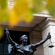 Photograph of a statue of Blind Justice outside the Albert V. Bryan United Sates Courthouse, autumn leaves in the foreground