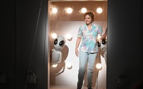 Kate McKinnon standing in the doorway of a spaceship with two gray aliens