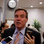 Mark Warner speaks as reporters hold up cellphones to record him.