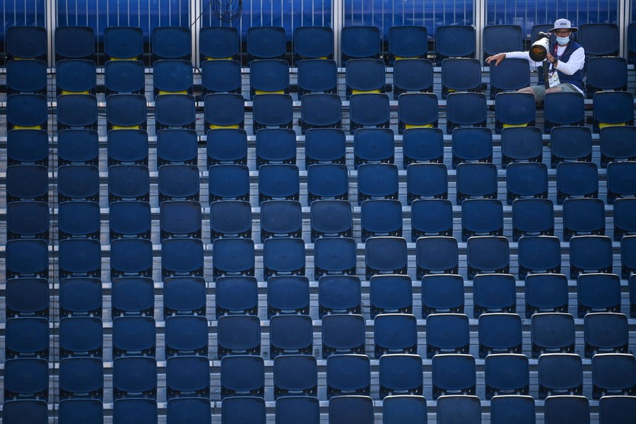 A single photographer sits in otherwise empty stadium stands.