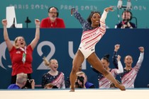 Teammates cheer in the background as a gymnast completes a floor-exercise routine.