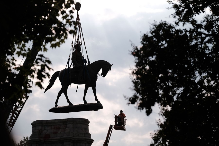 A statue of a Confederate soldier seated on a horse is lifted by a crane.