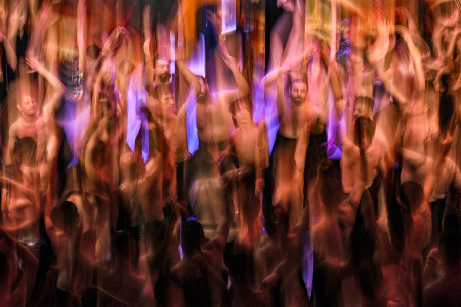 A blurred image of many shirtless men standing side by side with their hands raised