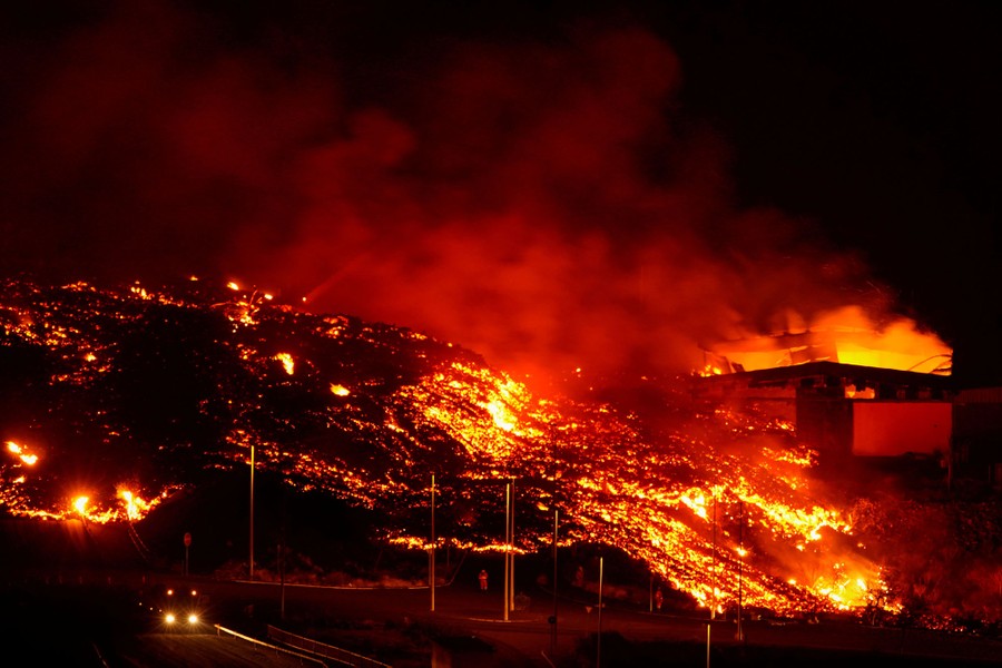 Lava flows over roads and buildings at night.