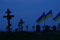 Photo of a cemetery with crosses and Ukrainian flags visible against a dark sky