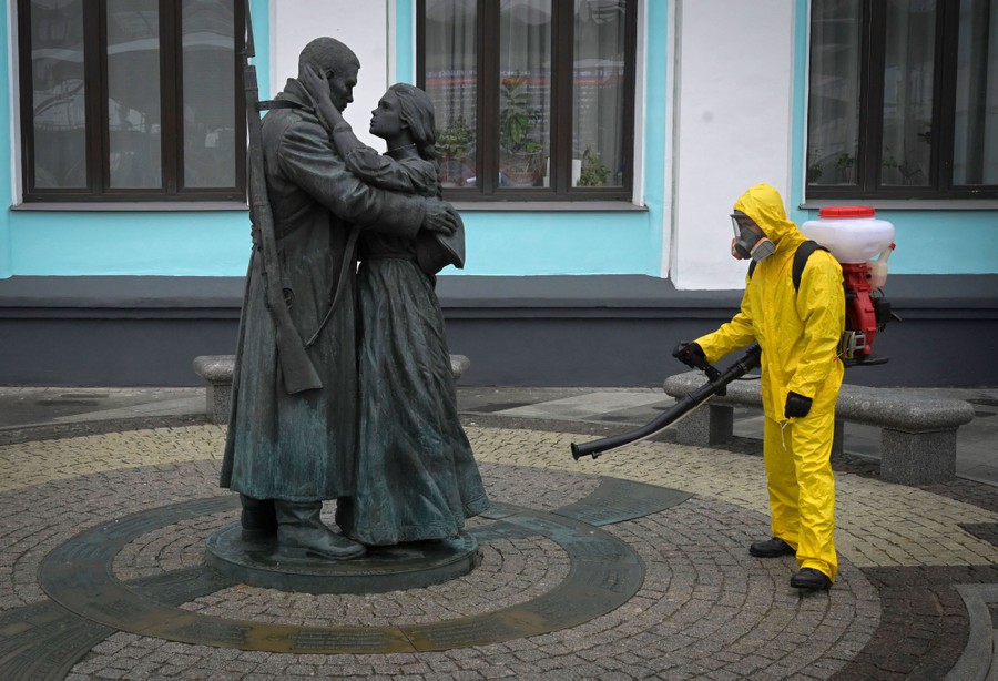 A person in protective gear sprays disinfectant onto the base of a statue.