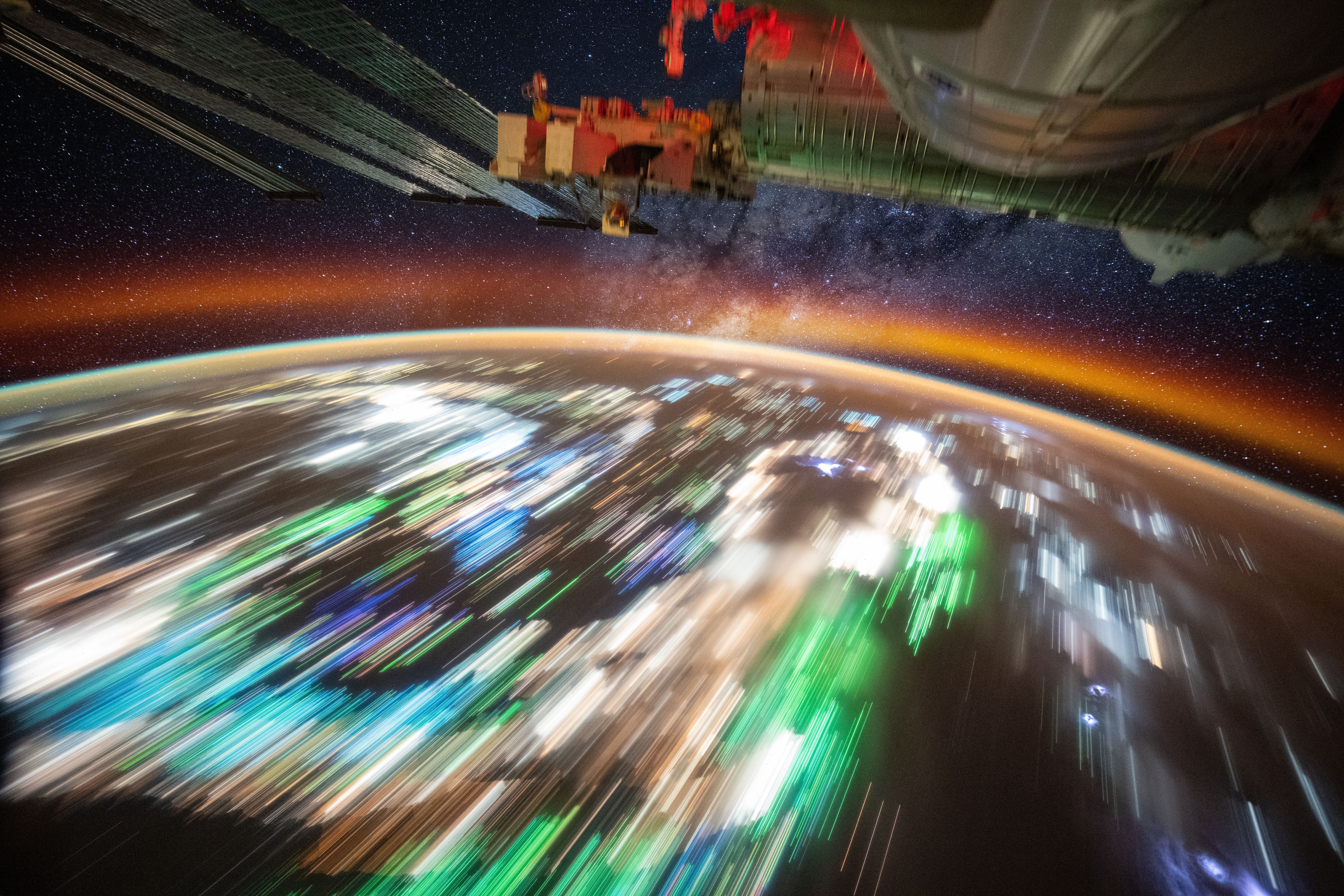Many-colored lights streak past below, in a long-exposure image from the ISS.