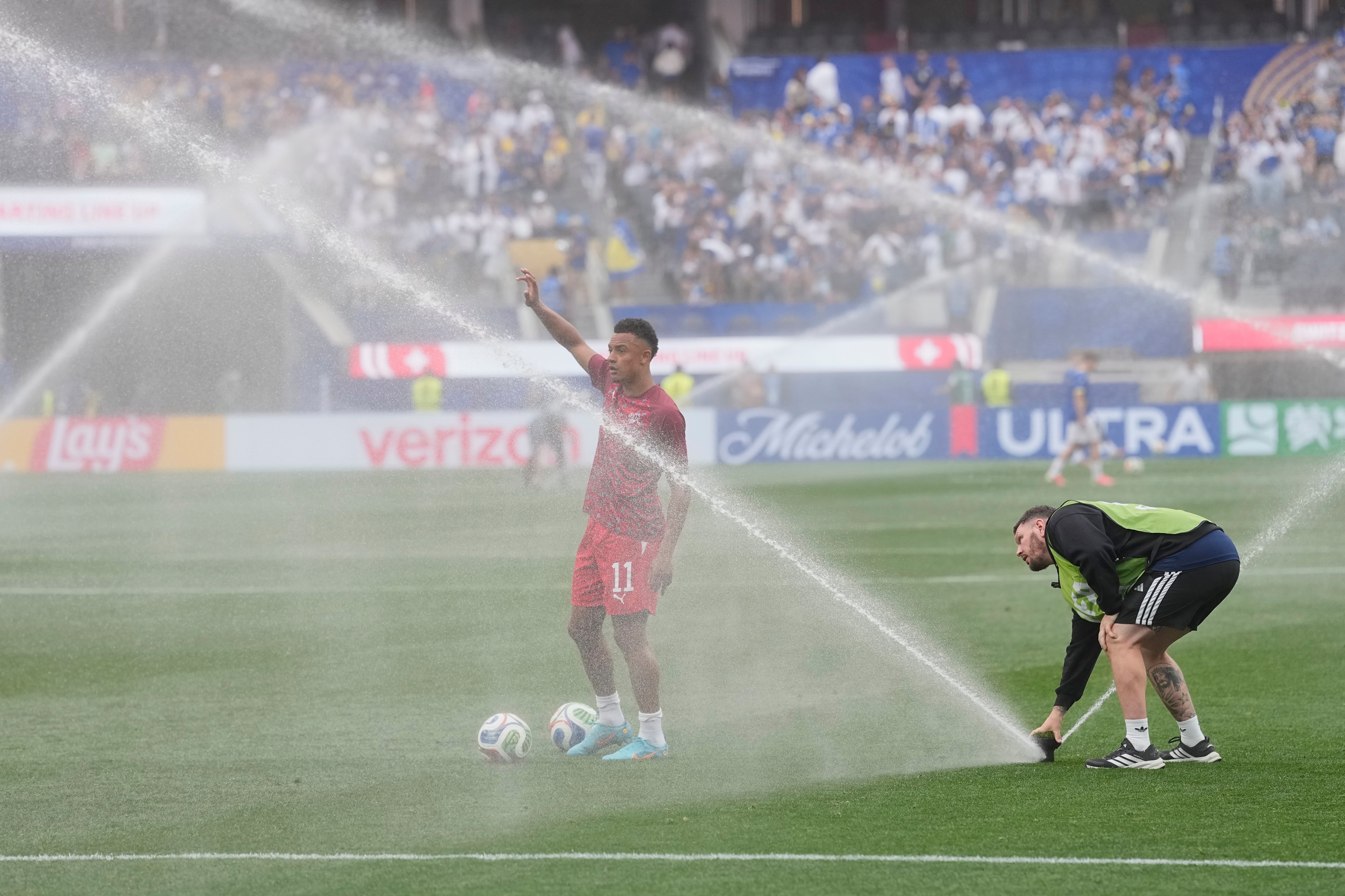 A soccer player tries to warm up as sprinklers water the field.