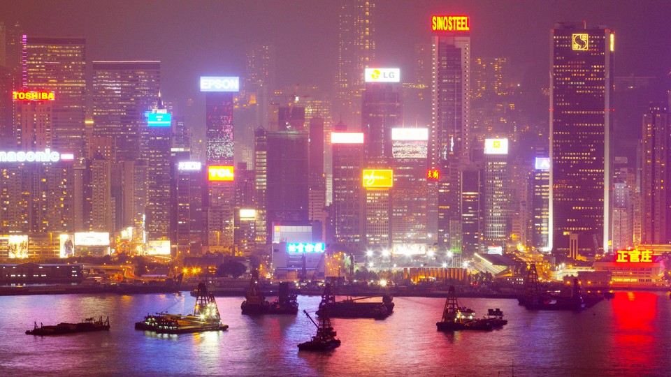 A bright city skyline illuminates fishing boats in a harbor.