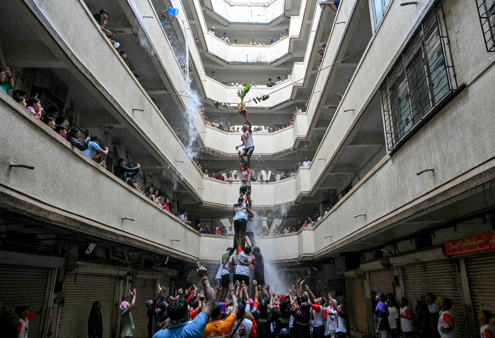 People form a tall human pyramid inside a multi-story atrium.
