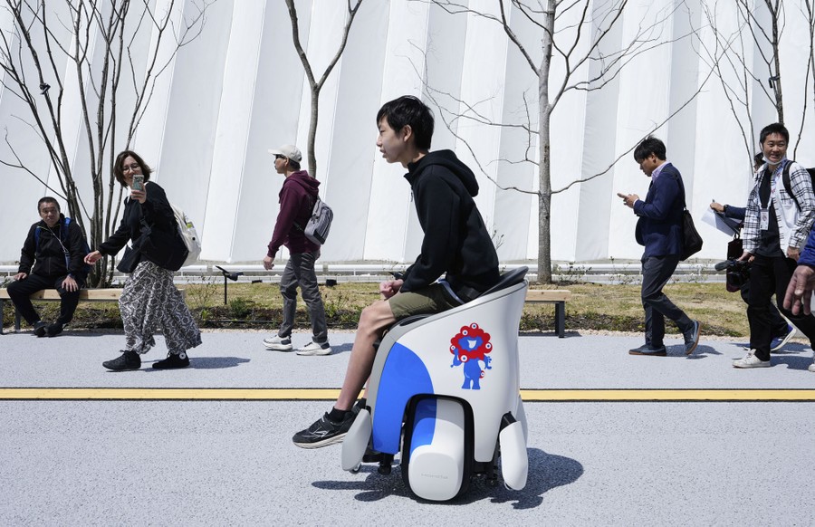 People watch as a person rides past, seated on a futuristic-looking mobility scooter.