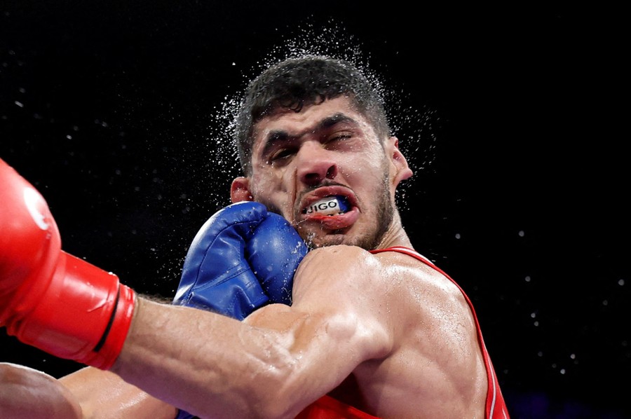 Droplets of sweat fly from the head of a boxer as his face is punched during a match.