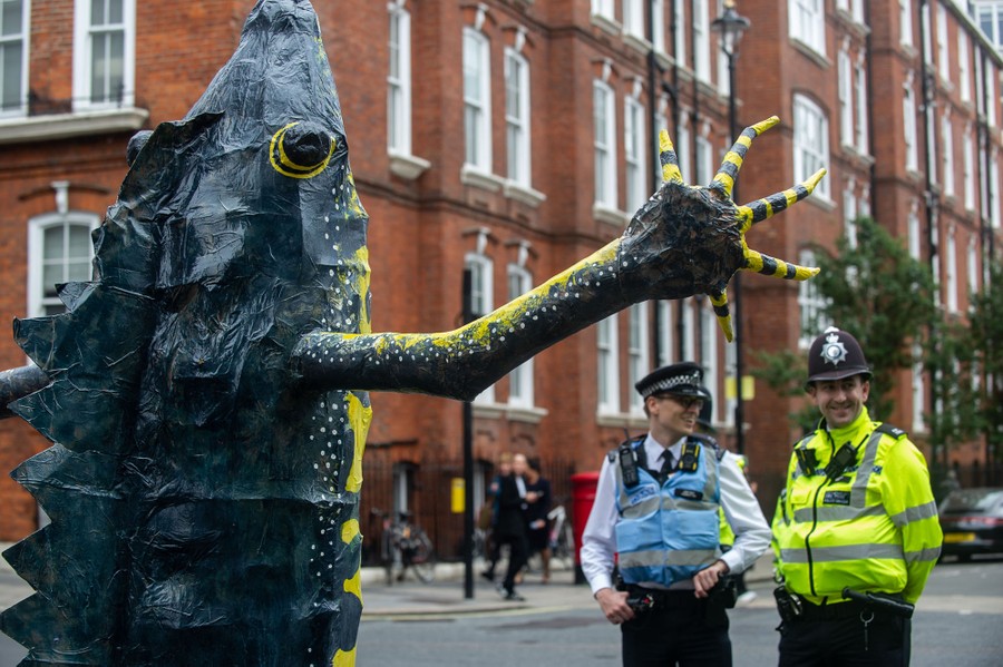 A protester wears an animal costume and gestures toward a pair of police officers.