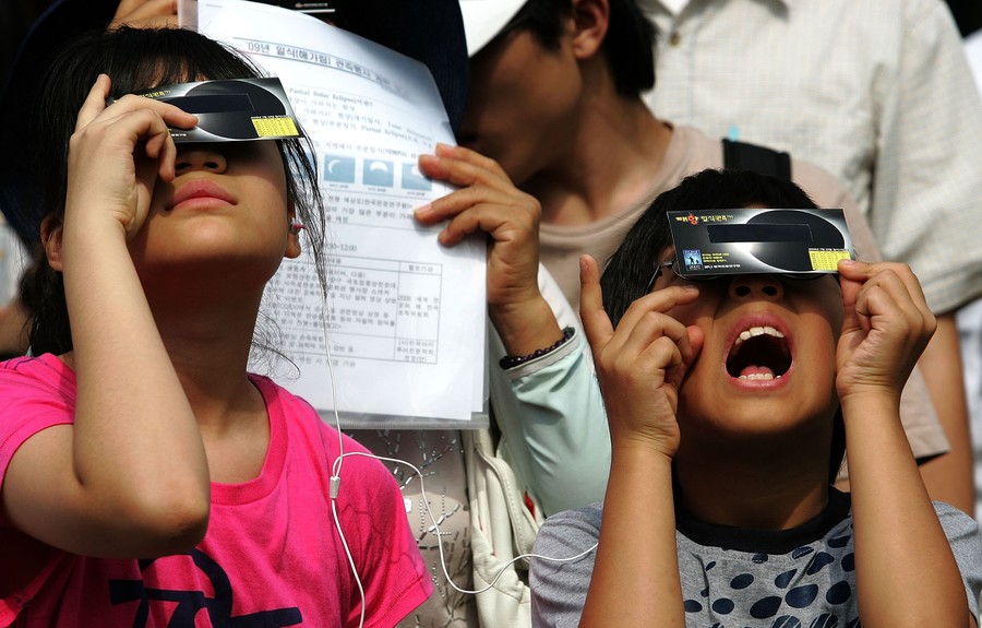 Young people look up toward the sun, wearing eclipse glasses.