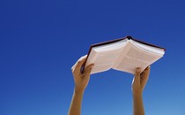 Young woman holding book up in air, low angle view