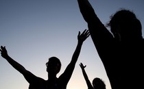 Silhouettes of people praying with their arms stretched up and out