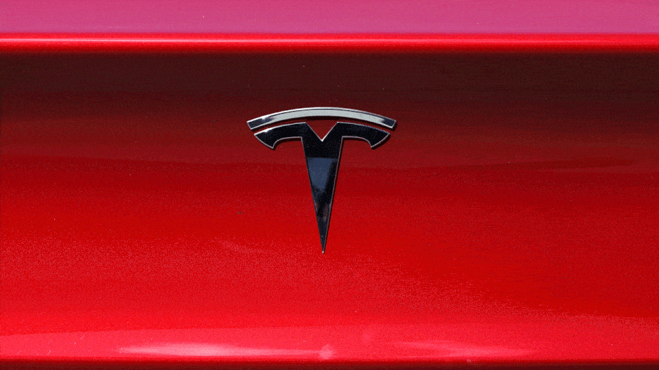 An animated illustration of a metal Tesla emblem repeatedly falling upside-down.