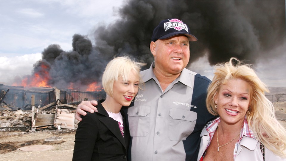 Dennis Hof poses with two blond women as a building burns.