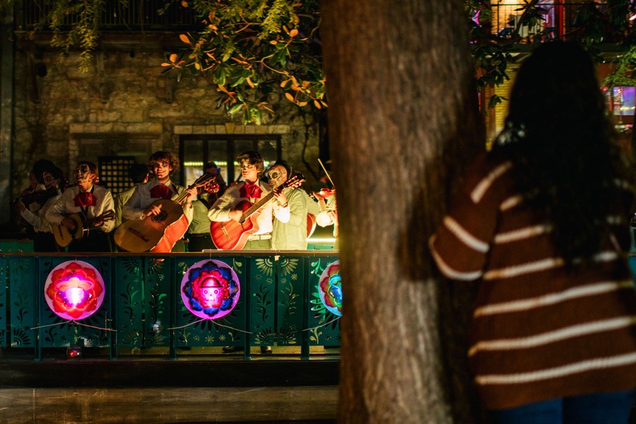 People watch as a Mariachi band passes by on a river in a city.