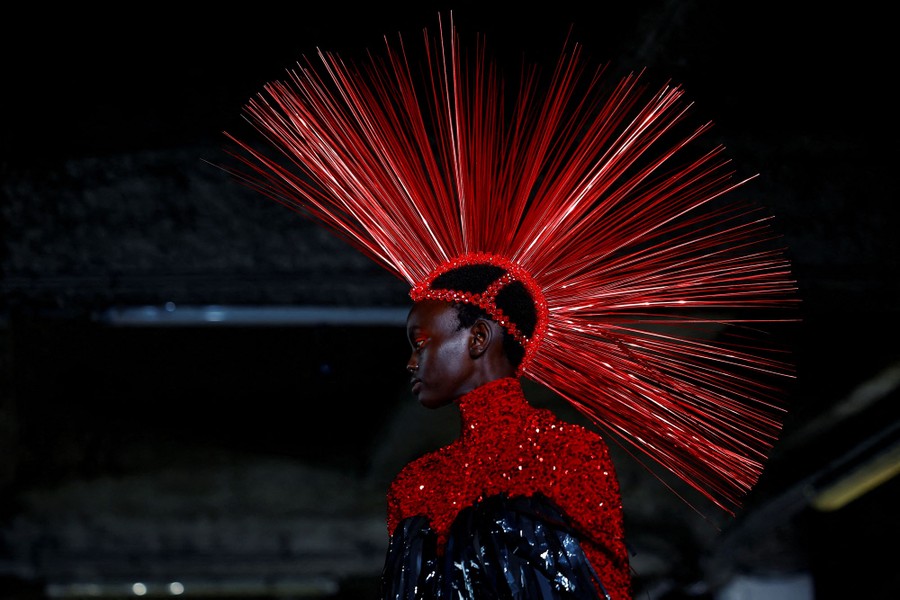 A model on a runway wears a hat that is decorated with many long red spikes.
