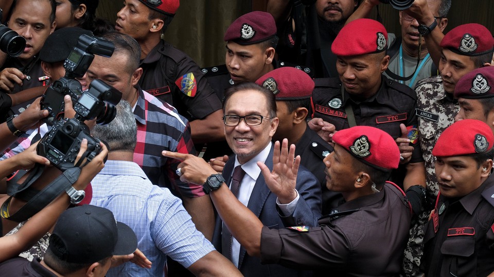 Anwar smiles and waves in between police officers and press photographers