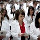 A group of students in white lab coats reads from pamphlets.