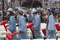 Four students walk in light blue commencement caps and gowns.