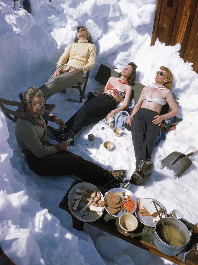 Four skiers sunbathe in the snow following a meal in Sun Valley, Idaho.