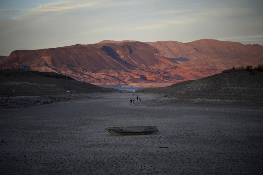 Several people walk on dry earth near an abandoned boat.
