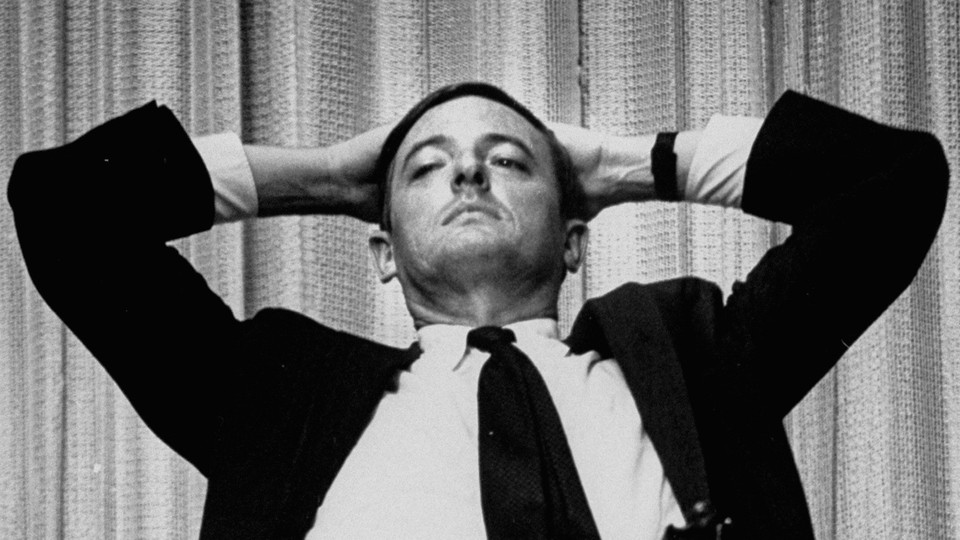 William F. Buckley sits with his hands placed behind his head.