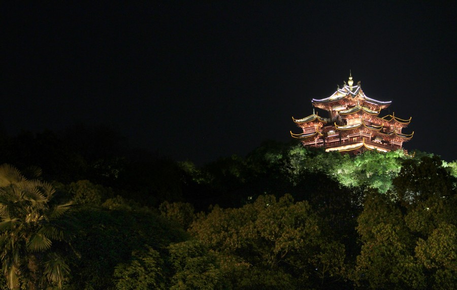 A nighttime view of an illuminated pavilion atop a hill, with multiple stylized balconies and roof structures.