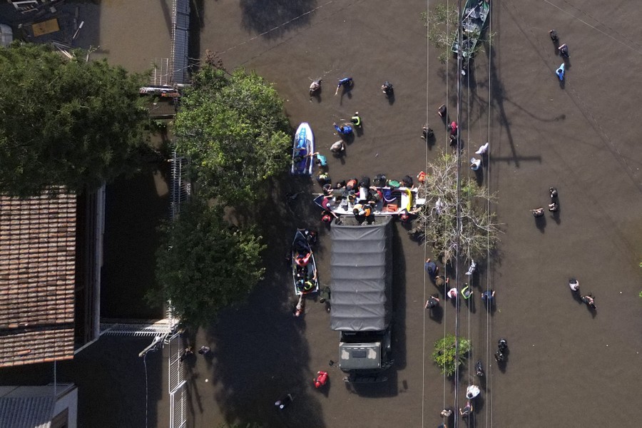 An overhead view of people rescuing others in a flooded area using small boats and a truck