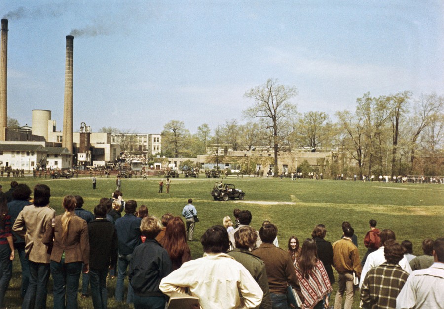 National Guardsmen drive a jeep on a grassy area, past protesters.