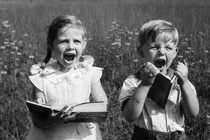 Two children in a field display extreme emotion while holding books.