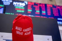 A red MAGA cap in front of a declining stock-market screen