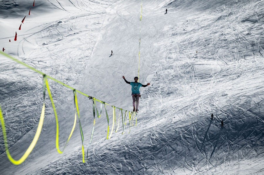A person walks on a slackline high above a ski slope.