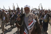 Houthi fighters march with weapons pointed in the air, a white-bearded militia member in the foreground.