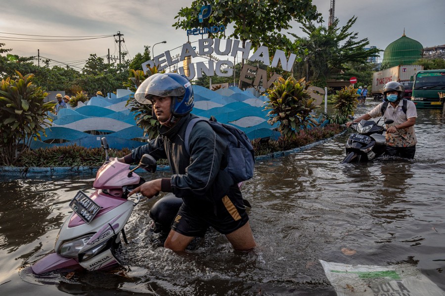 Two people push motorbikes through thigh-deep floodwater.