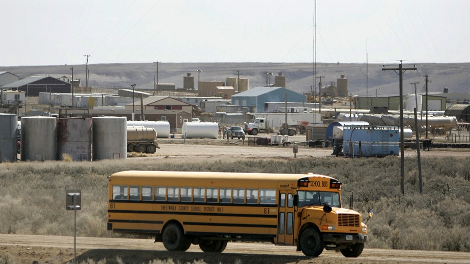 A yellow school bus drives down a dusty road with rolling plains in the background.