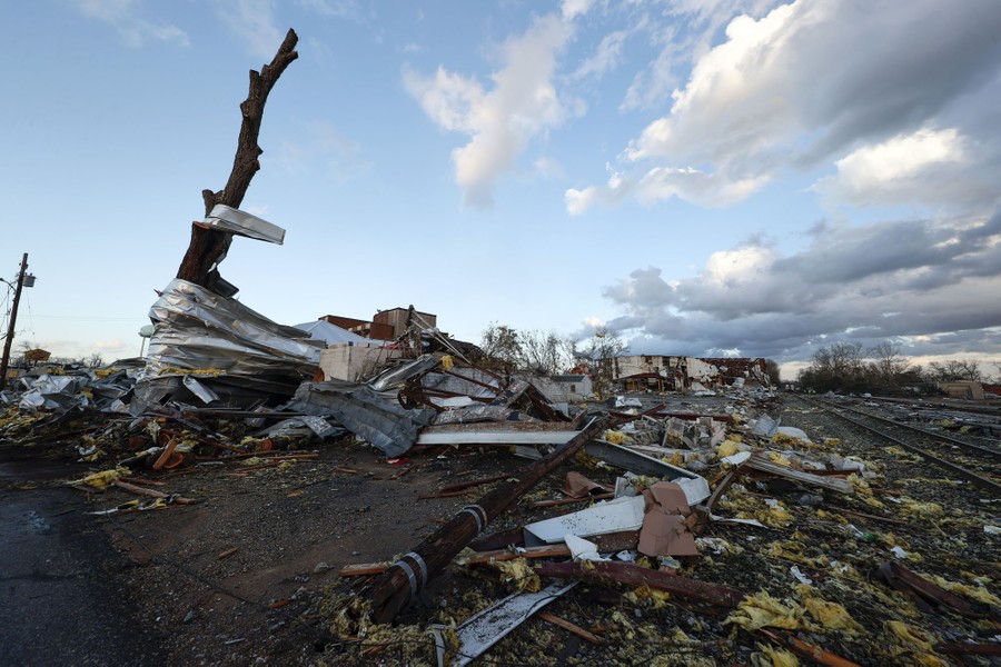 Wet, windblown debris lies scattered among broken trees, damaged buildings, and railroad tracks.