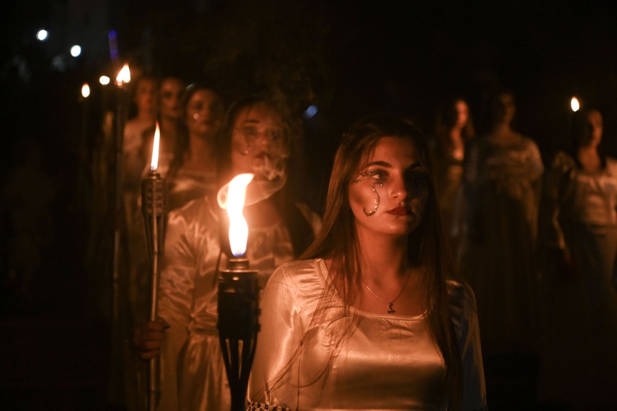 Two lines of women in costume hold torches during a festival.