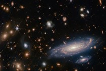 An image of deep space, showing numerous galaxies of varying sizes and shapes, featuring a pair of larger spiral galaxies at lower right