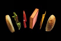 A book floats in the air between two buns, a piece of lettuce, two tomato slices, and American cheese.