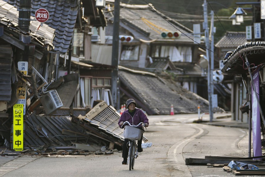 A person rides a bike past quake-damaged houses.