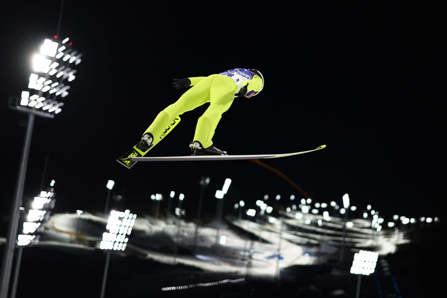 A ski jumper is seen in midair at night with an illuminated course seen below.